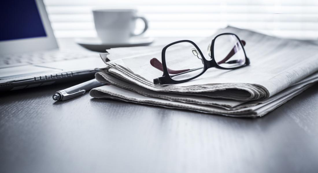Brille auf Zeitung vor Laptop neben Stift und Kaffeetasse