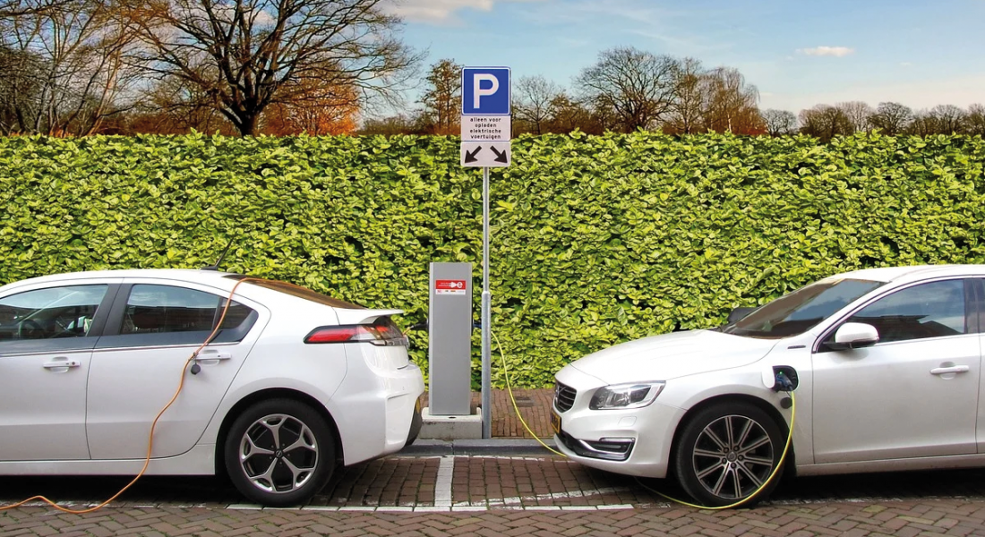 Zwei Autos an Ladestation vor grüner Hecke