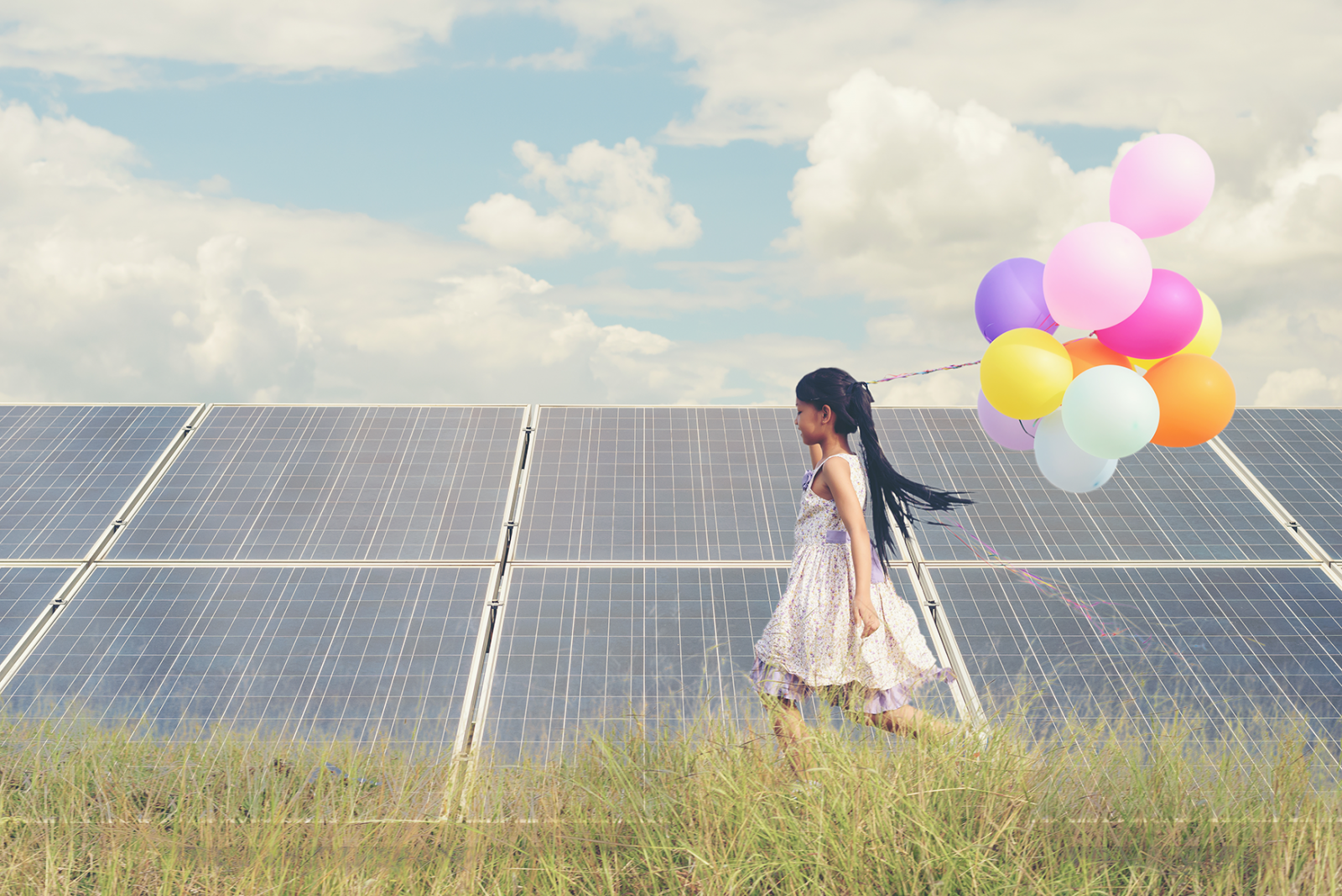 Kleines Mädchen läuft über die Wiese in der Hand bunte Luftballons im Hintergrund Solarpannels