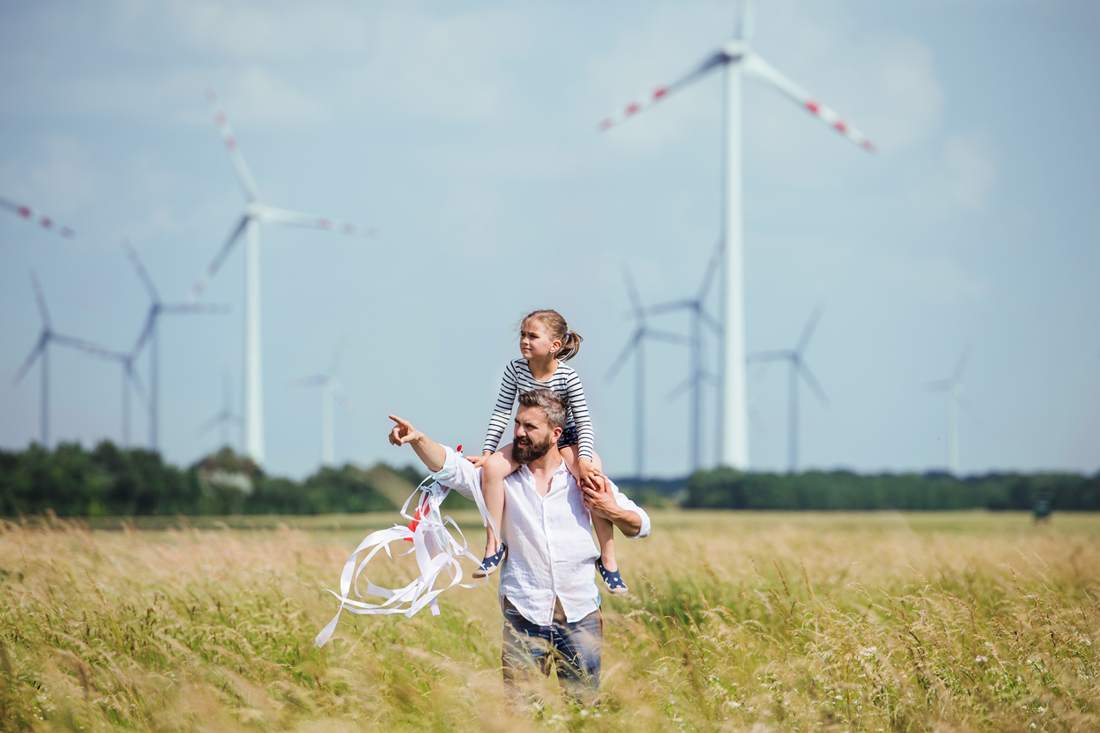 Papa hat seine kleine Tochter auf der Schulter im Feld im Hintergrund Windräder