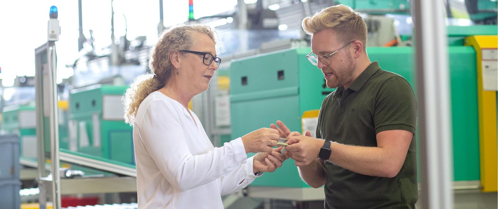 Frau und Mann stehen in der Produktion und schauen sich zusammen ein Bauteil an