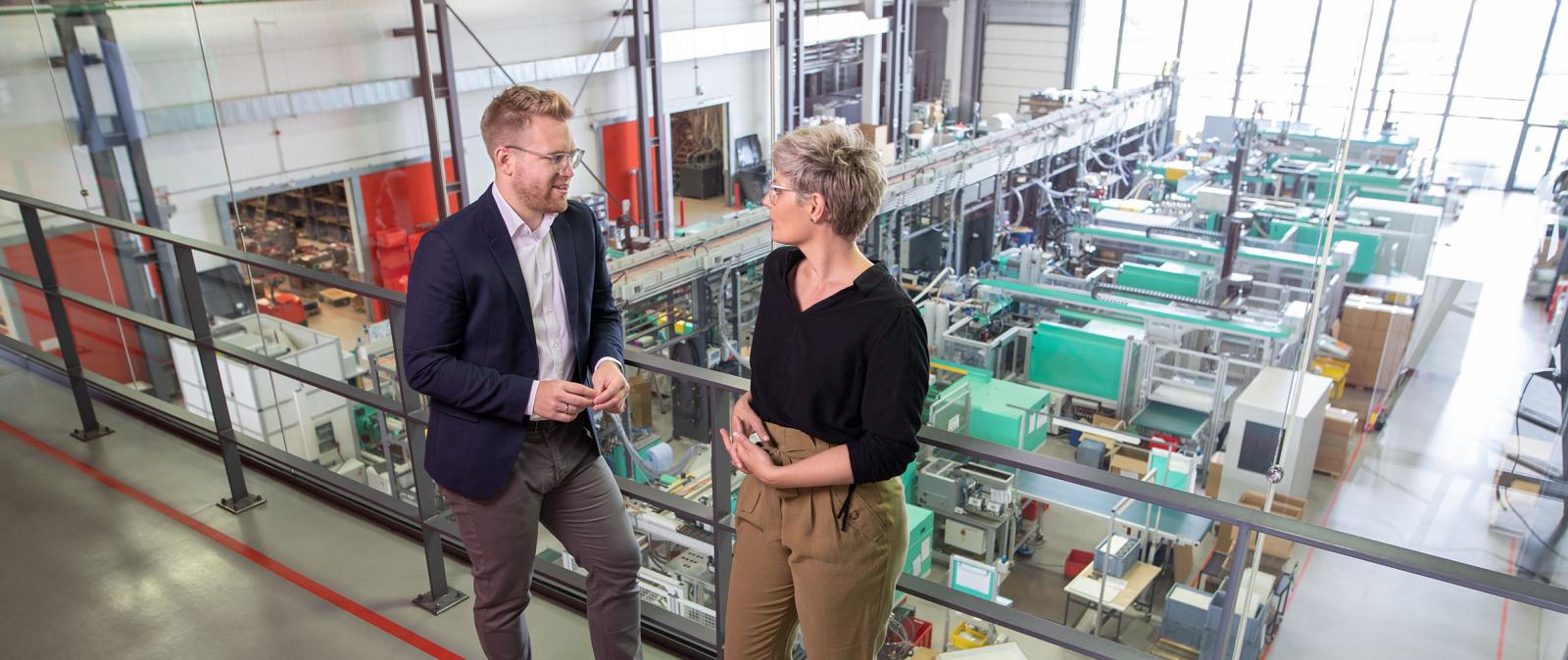 Frau und Mann auf einer Galerie im Hintergrund die Produktion