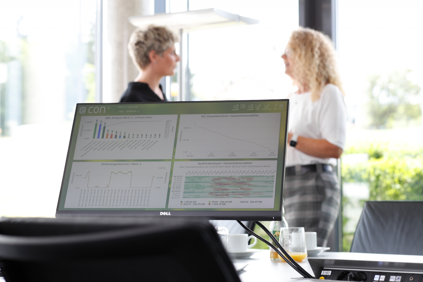 Softwarescreen, im Hintergrund zwei Frauen im Gespräch