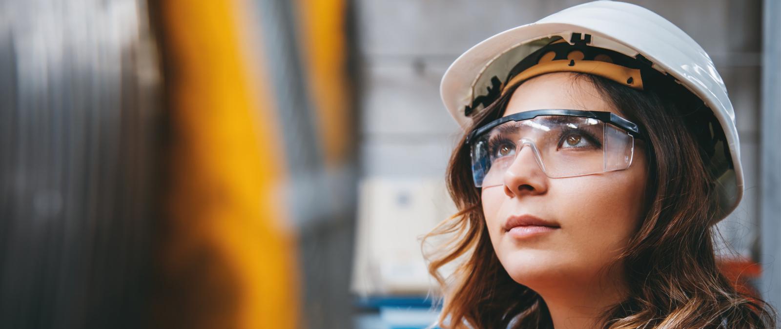 Close-up vom Gesicht einer Fabrikarbeiterin mit Schutzbrille und Helm
