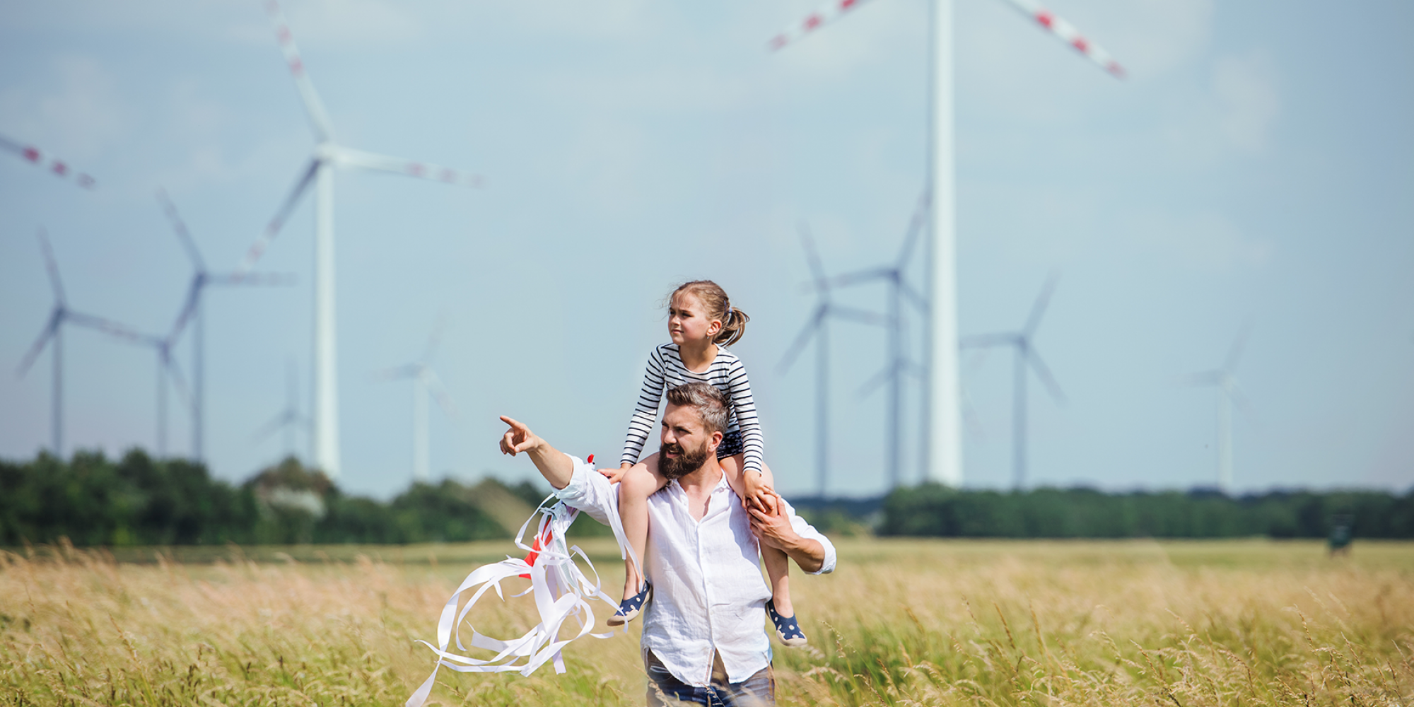 Papa hat seine kleine Tochter auf der Schulter im Feld im Hintergrund Windräder