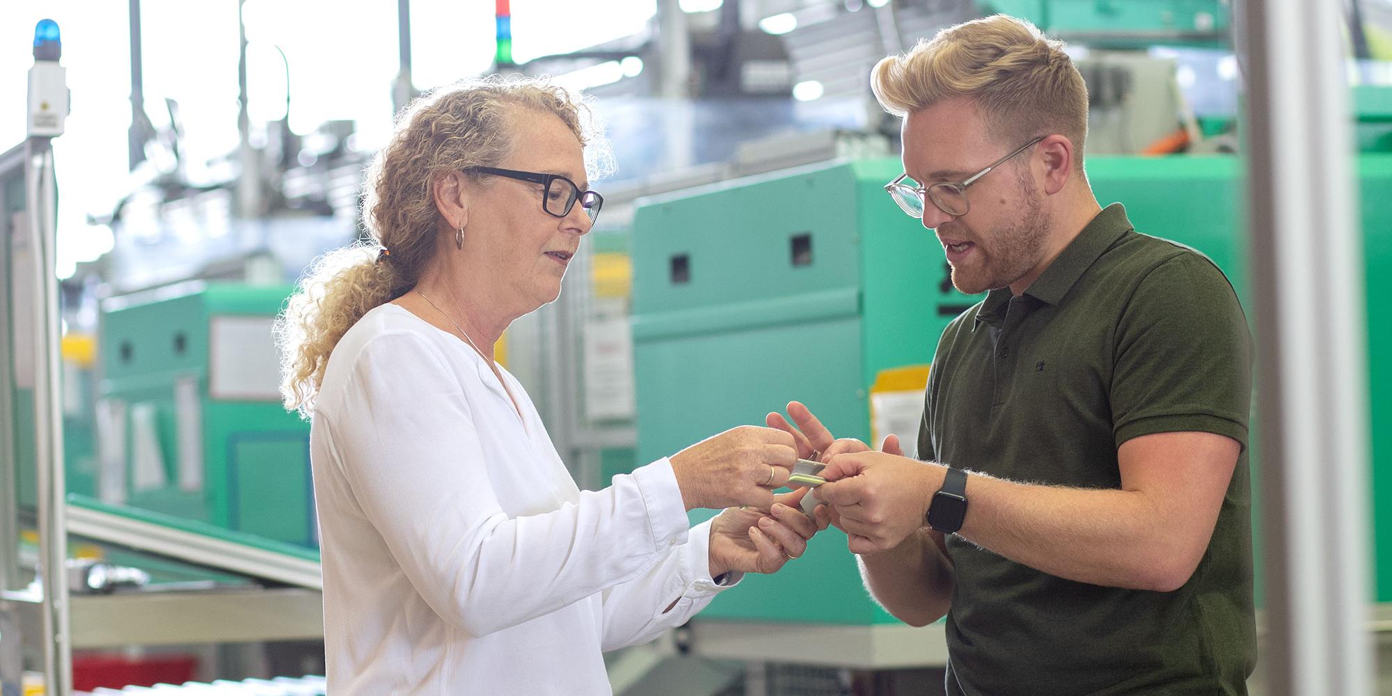 Frau und Mann stehen in der Produktion und schauen sich zusammen ein Bauteil an