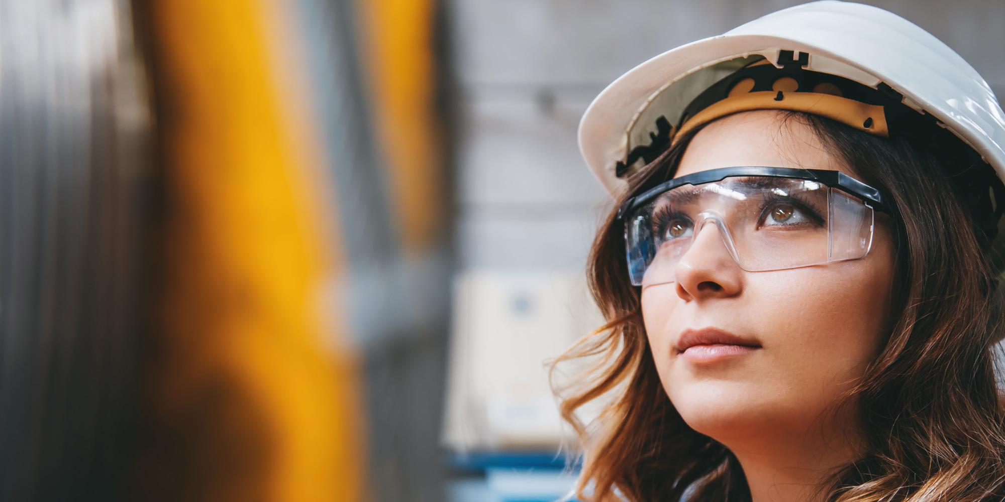 Close-up vom Gesicht einer Fabrikarbeiterin mit Schutzbrille und Helm