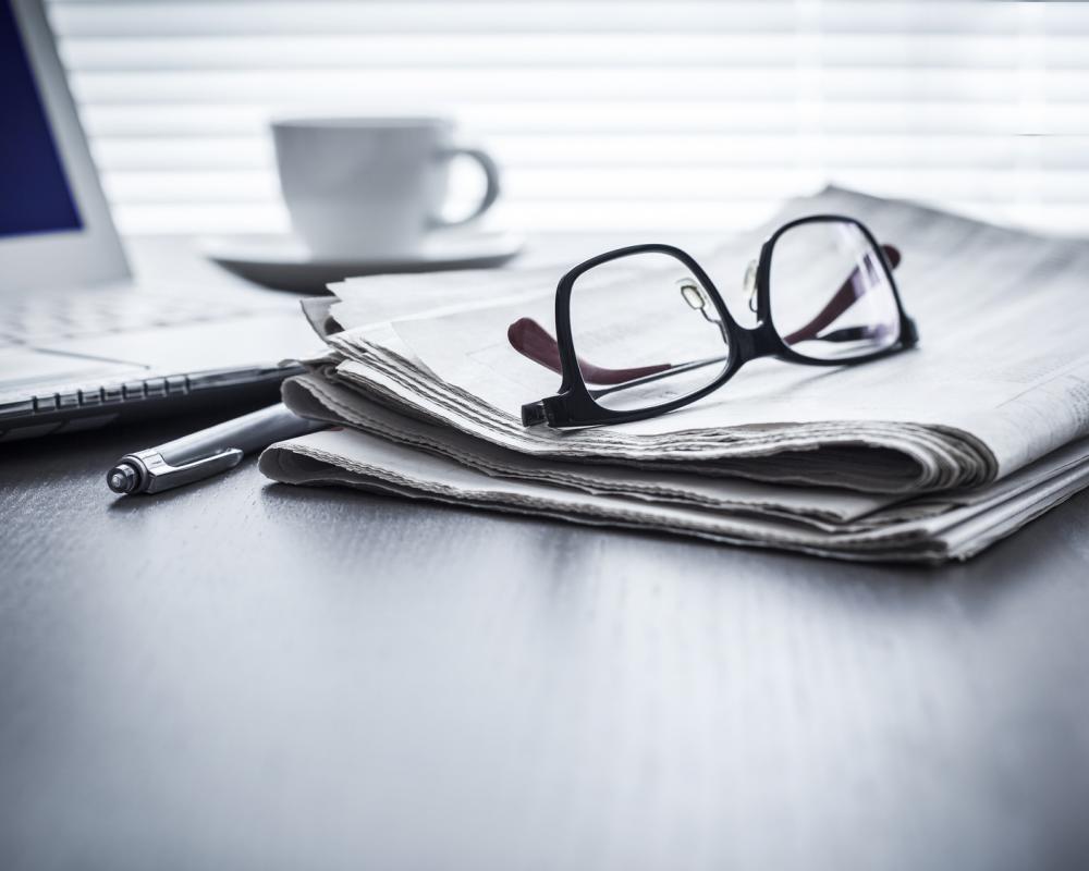 Brille auf Zeitung vor Laptop neben Stift und Kaffeetasse