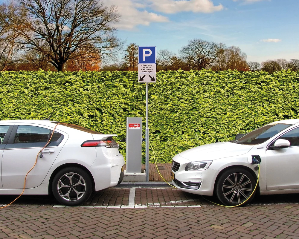 Zwei Autos an Ladestation vor grüner Hecke