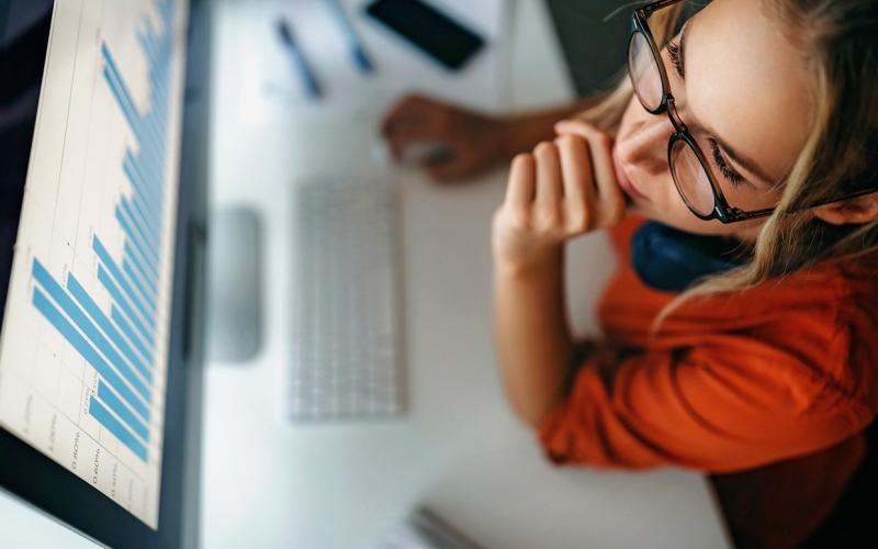 Frau mit Brille sitzt vor Computermonitor darauf zu sehen Diagramme