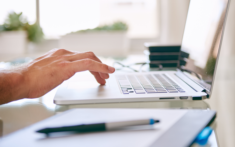 Hand auf Laptopmouse daneben Stift auf Unterlagen