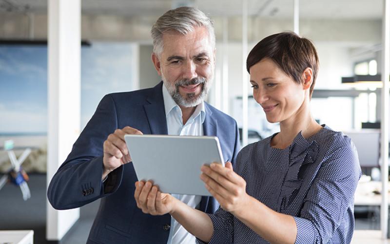 Mann und Frau schauen während Gespräch im Büro auf Tablet