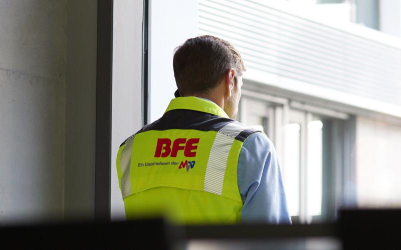 Mann mit gebrandeter Weste steht vor dem Fenster und telefoniert