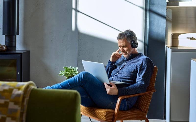 Homeoffice Mann sitzt gemütlich im Stuhl und schaut in den Laptop